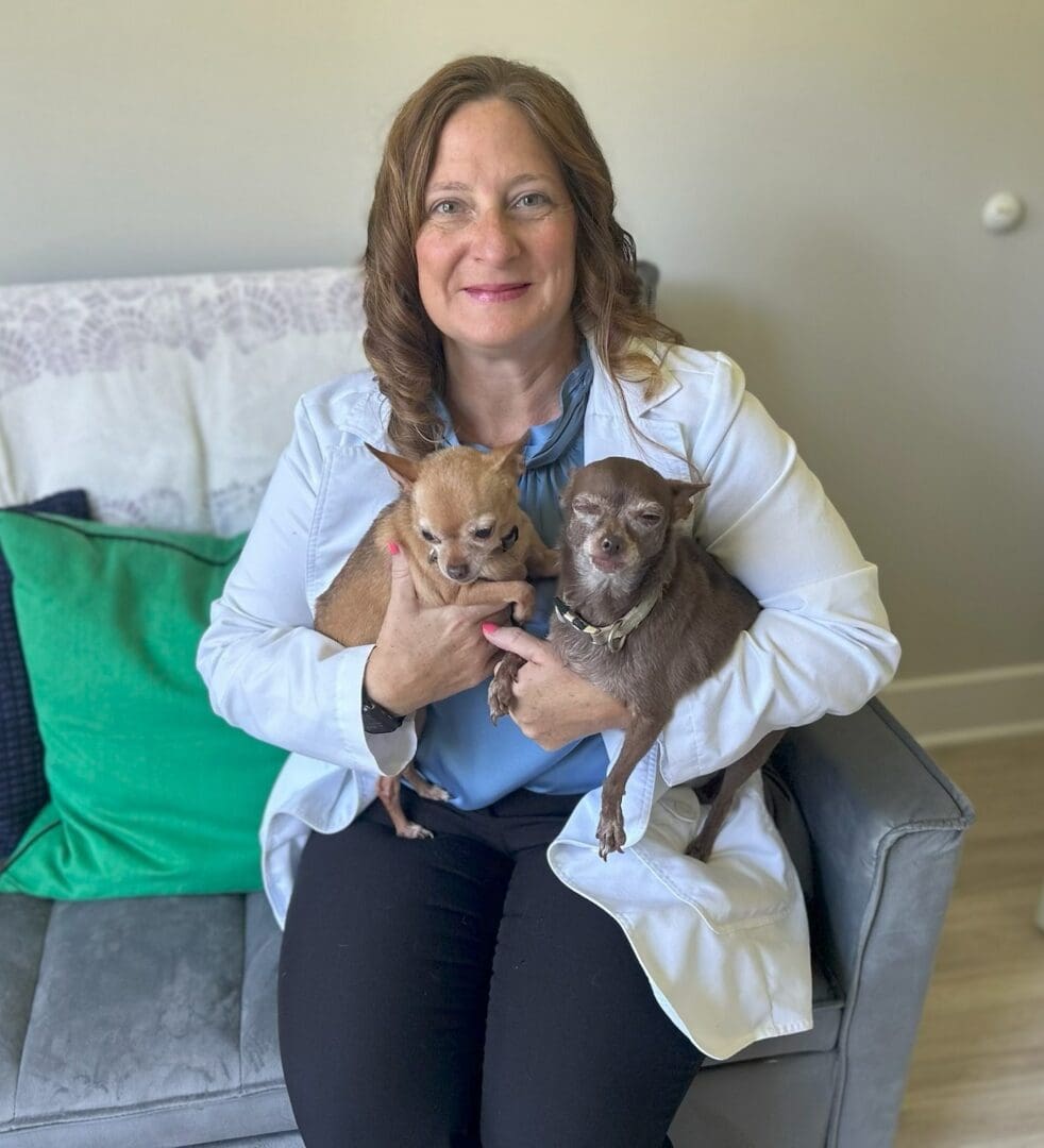 Woman in white coat holding two small dogs